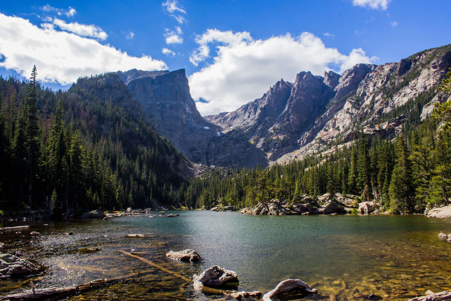 lake with trees around in the background and mountains against a blue sky