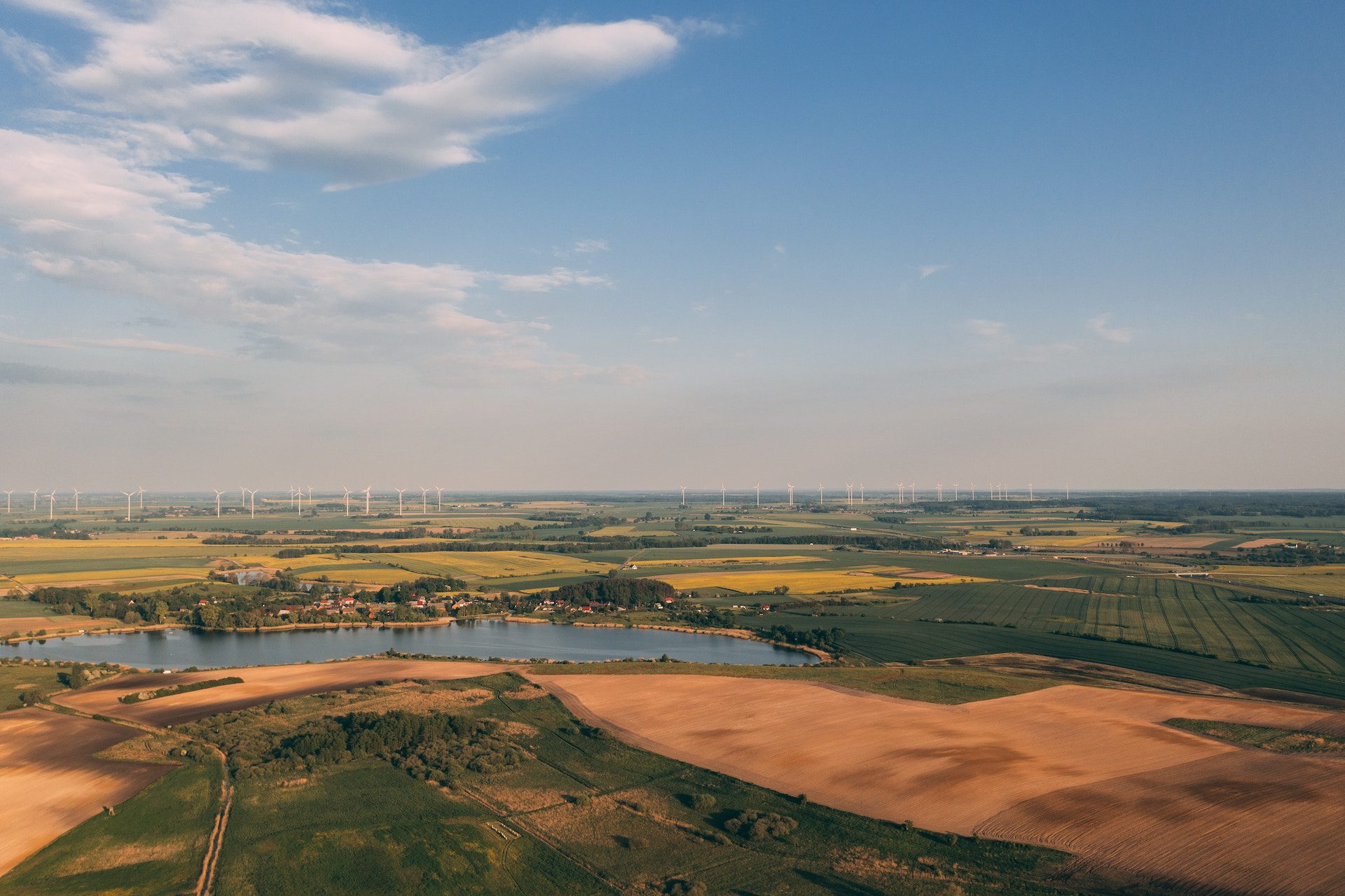 view of fields and a lake with a row of wind turbines in the distance