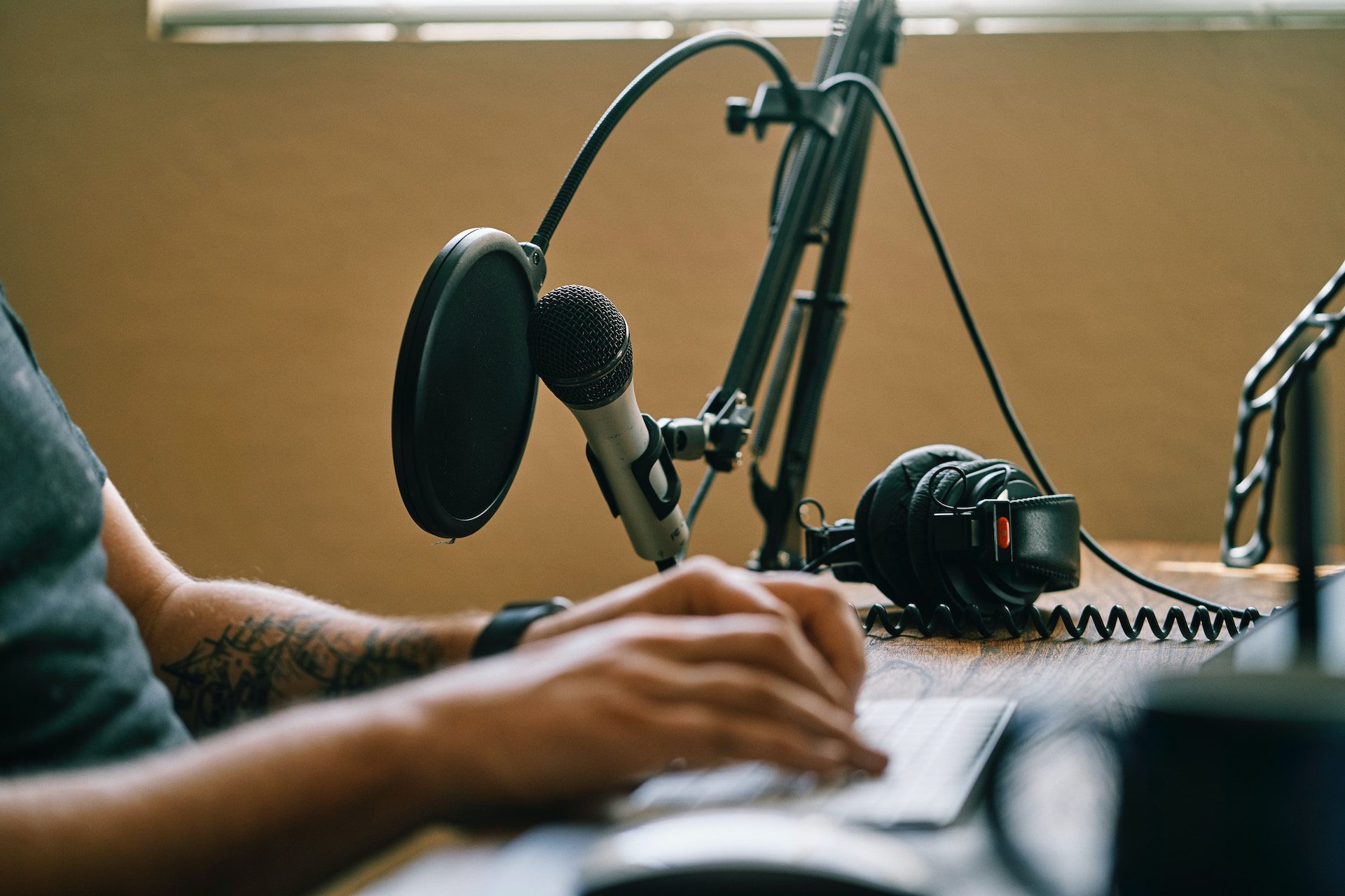 hands typing on the keyboard with a microphone and headphones next to the hands