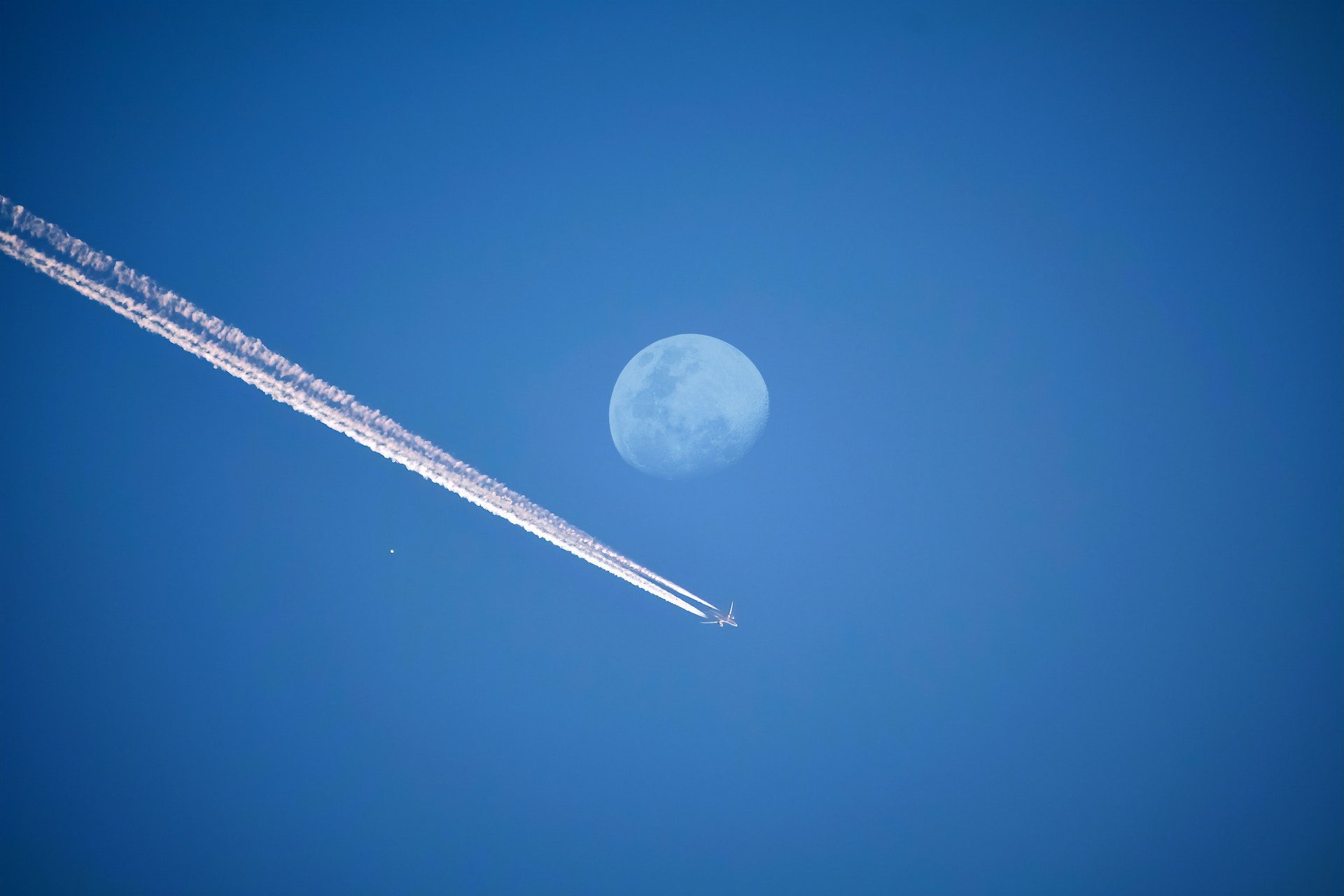 aeroplane flying through the blue sky underneath a moon