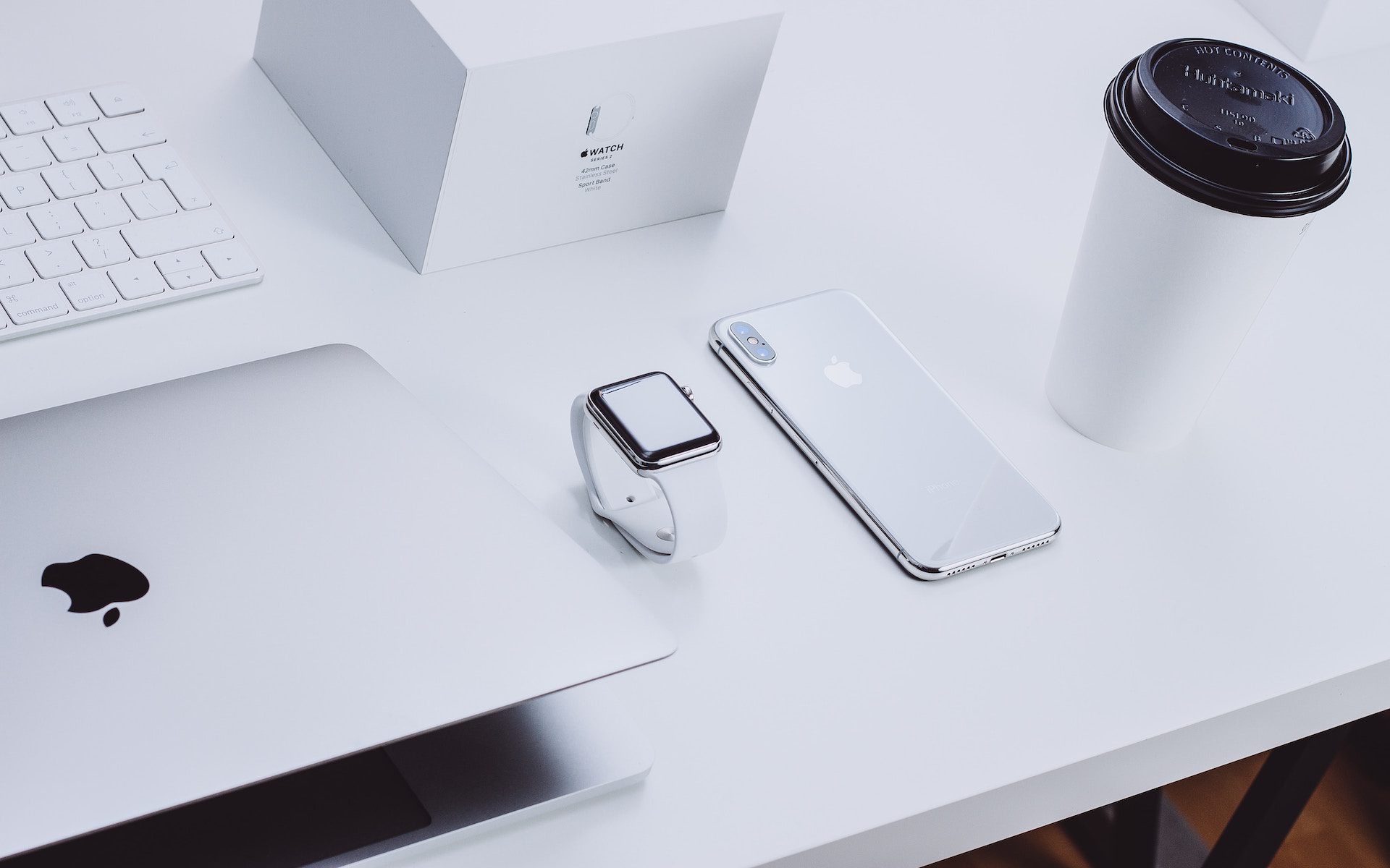 iphone, apple watch and laptop on a white desk with a white coffee cup