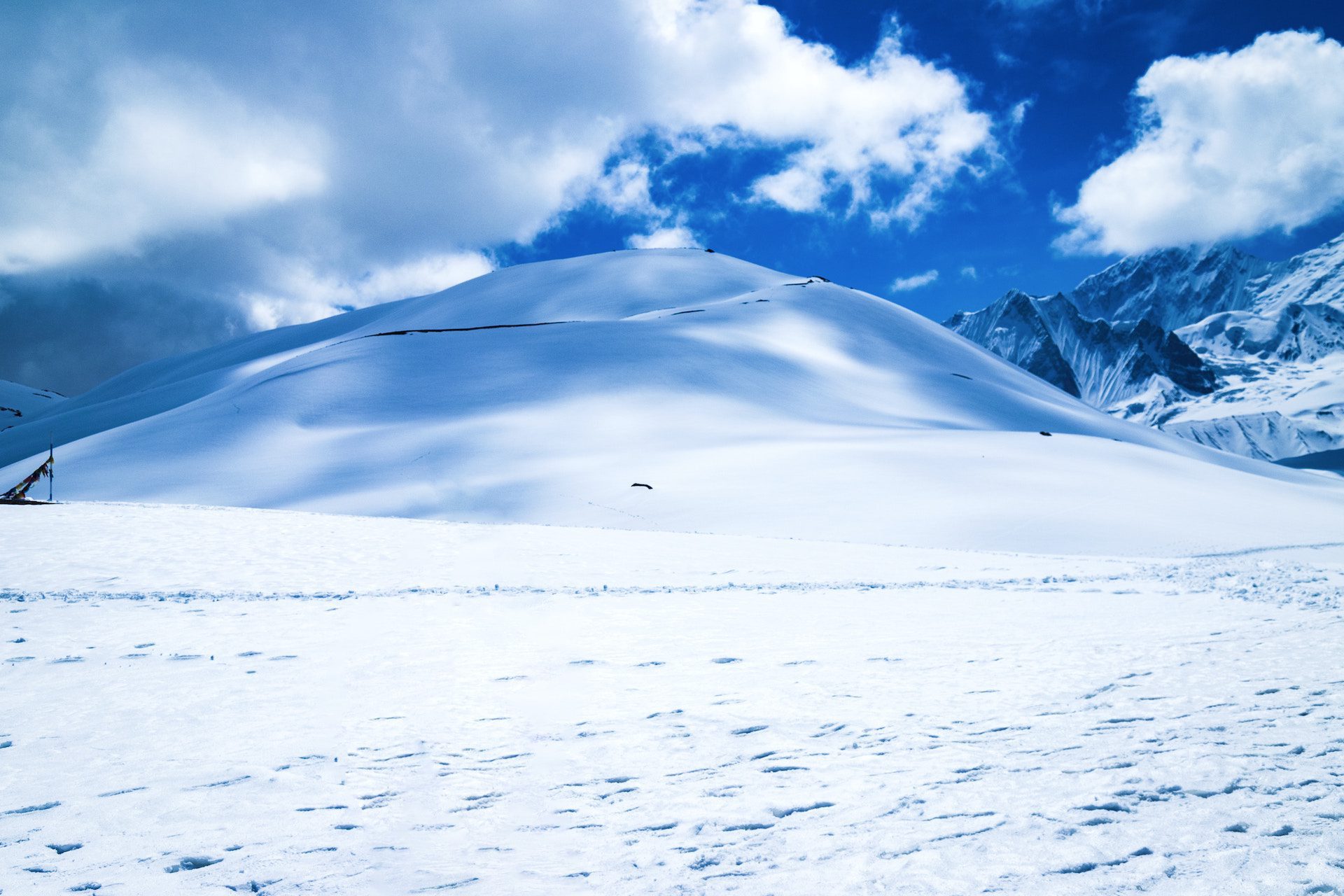 snow on the ground with a snow covered hill and mountains in the background against a blue sky with clouds