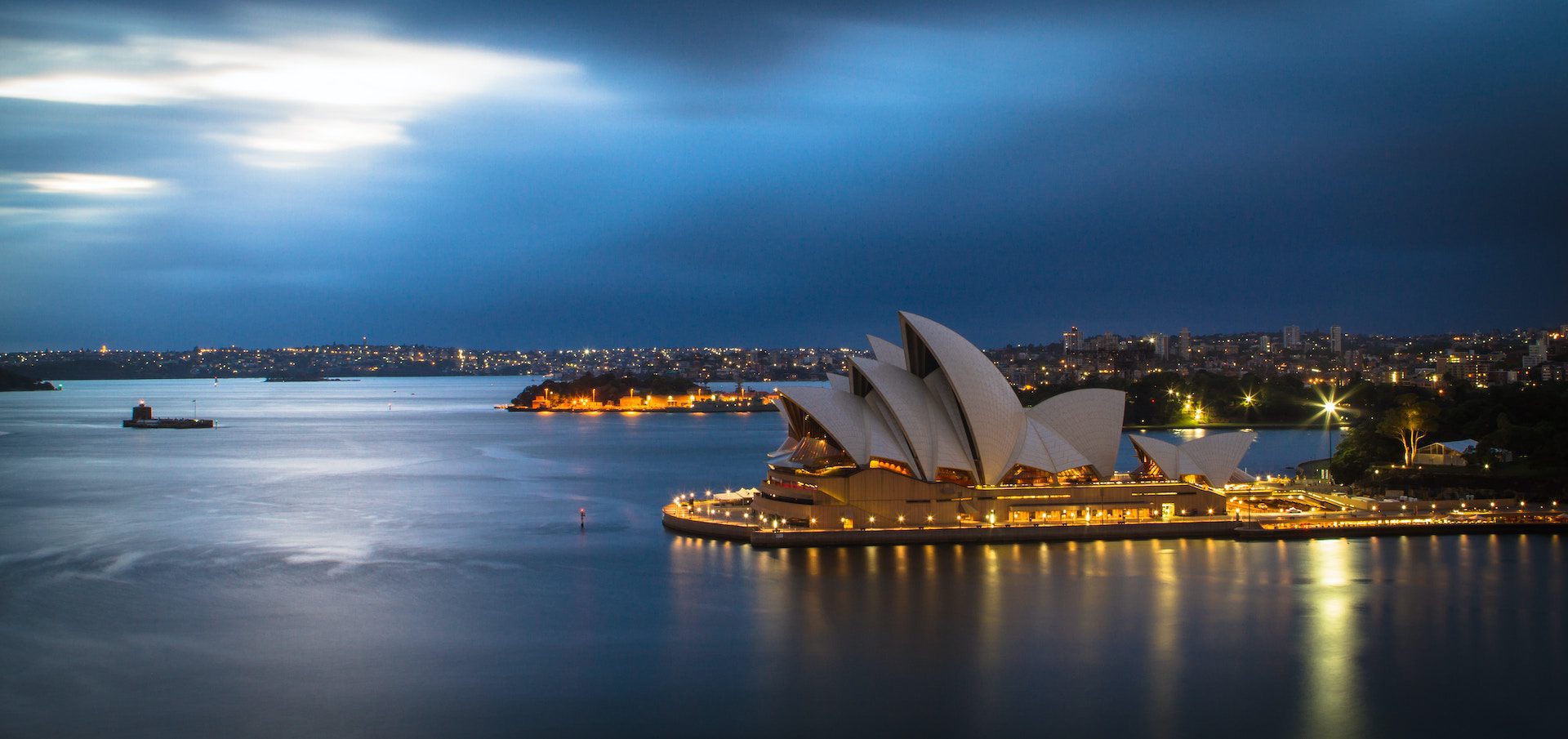 Sydney Opera House in the evening lit up with view of the ocean and buildings in the background
