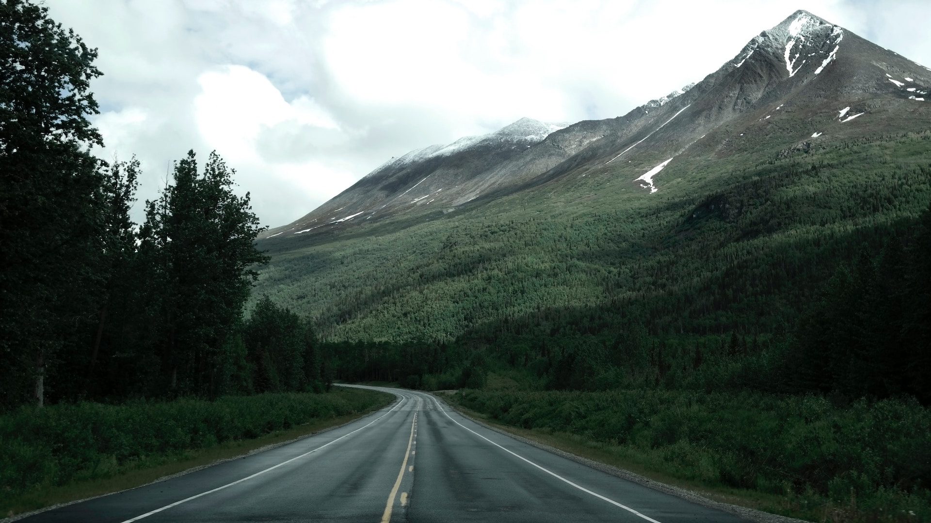 view of a road with mountain in the background and trees and grass either side