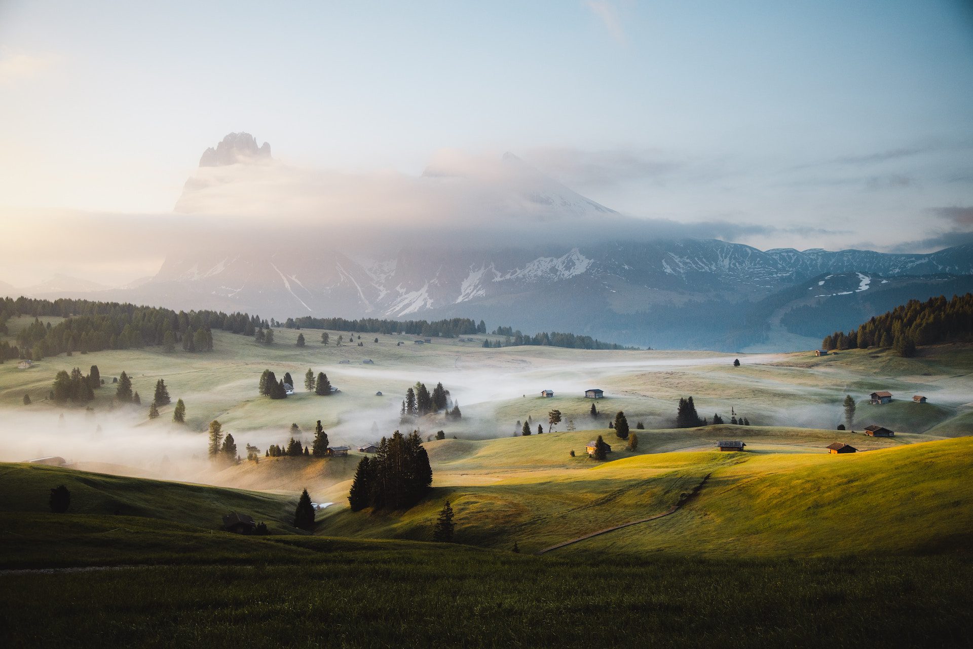 rolling green hills with trees and mist and view of mountains in the background