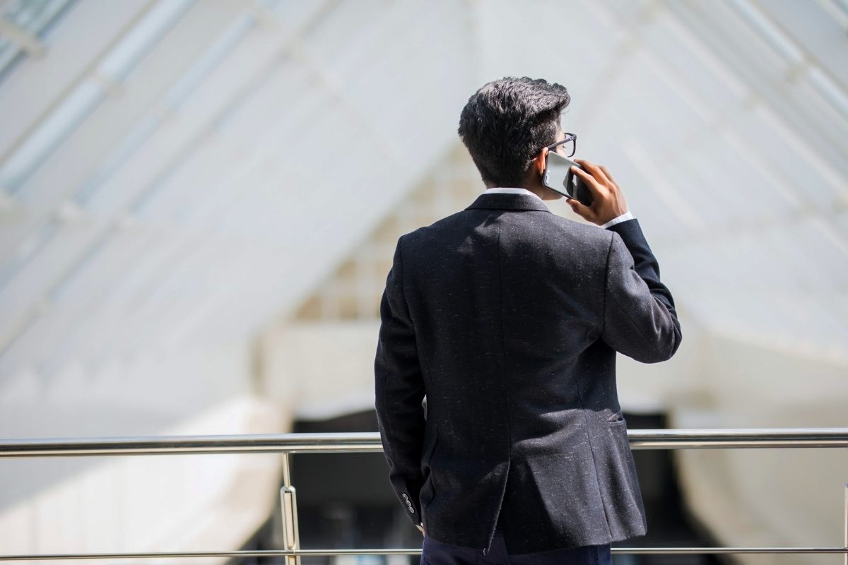 A businessman in a suit talks on a smartphone while standing in a modern building