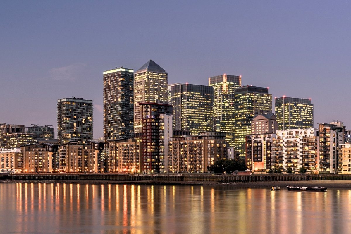 A view of a Canary Wharf skyline at dusk, with illuminated skyscrapers reflecting in the river Thames