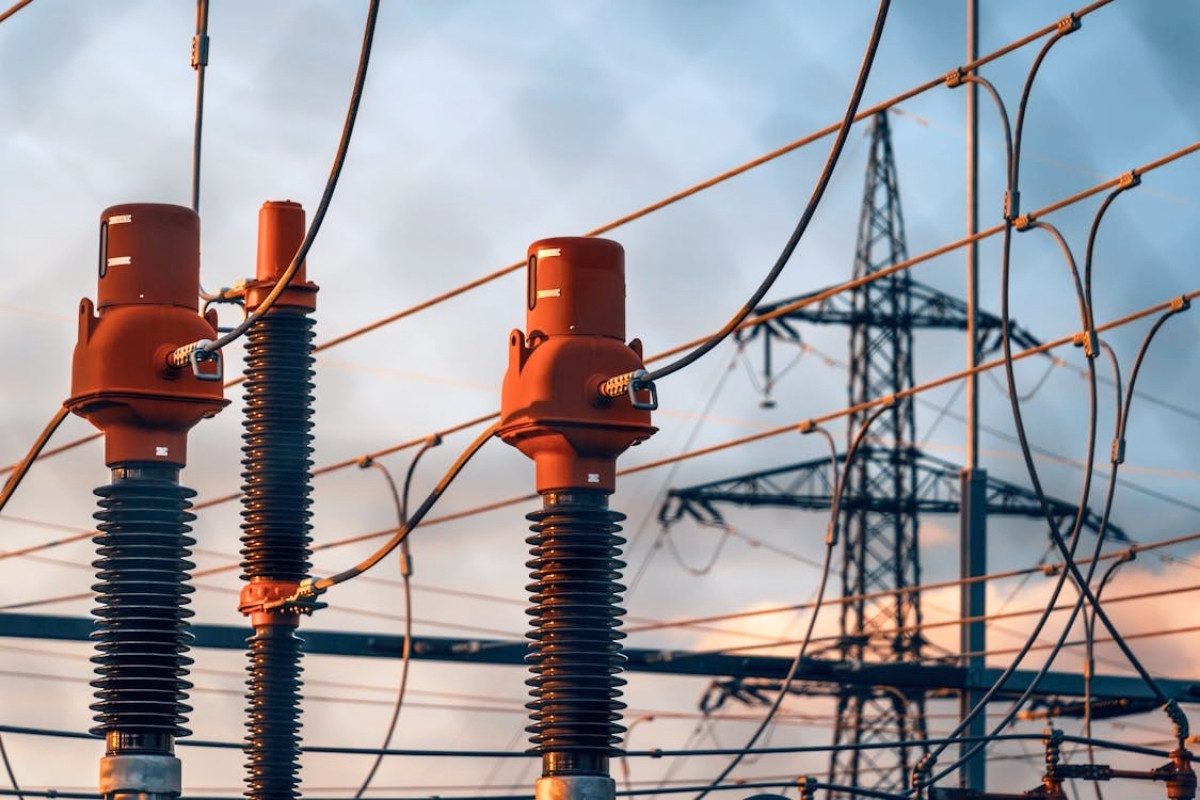 Close-up of three large, red-capped electrical insulators in the foreground with a pylon in the background