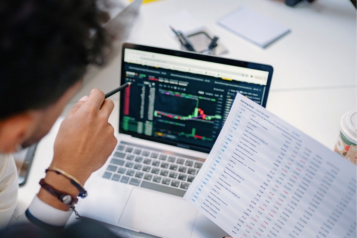 Two people review financial data on a laptop screen and a printed spreadsheet