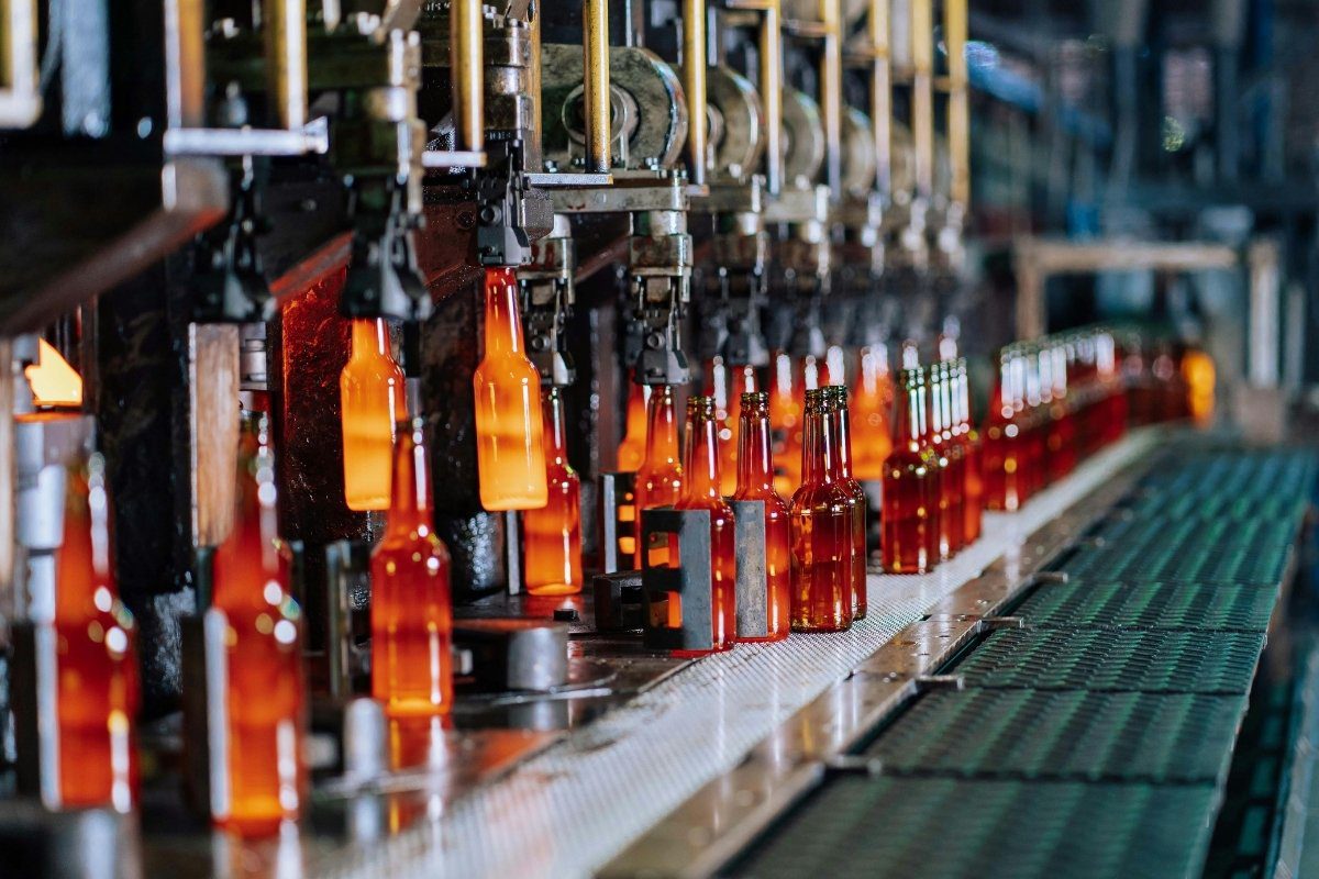 Molten glass bottles are formed and cooled on an industrial conveyor belt in a factory