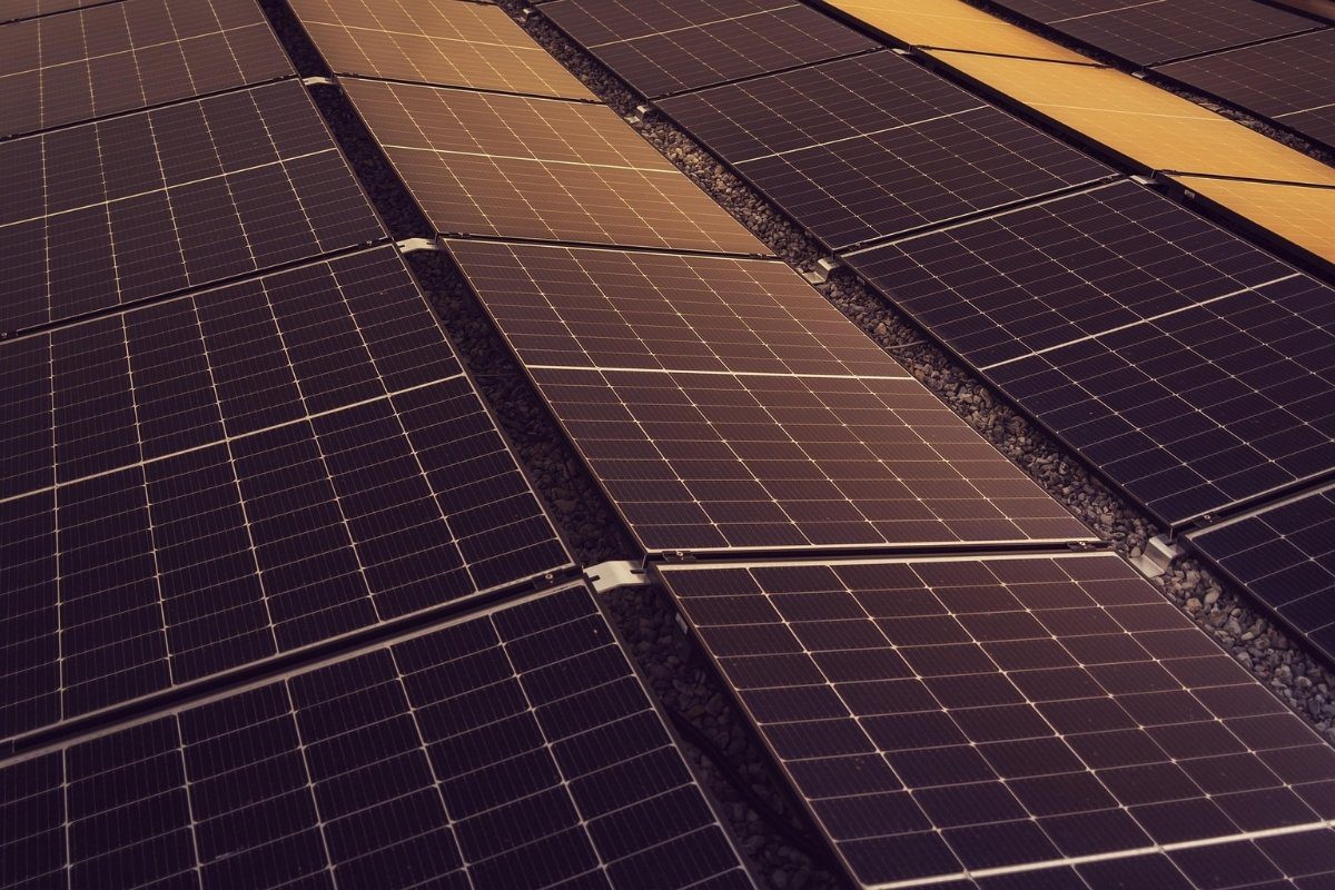 Rows of solar panels generating electricity angled upwards, with some panels reflecting sunlight